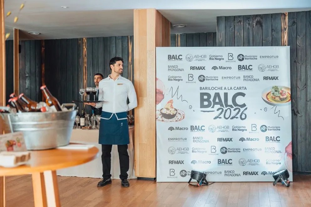 Mozo con una bandeja de copas junto al panel de Bariloche a la Carta 2026