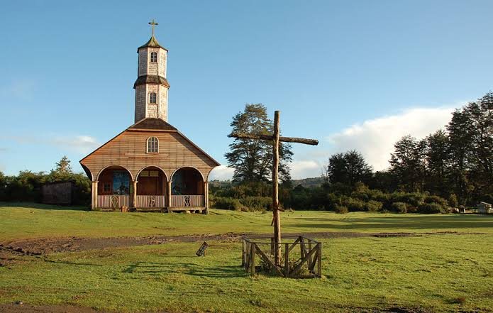 Iglesia de madera de Chiloé con cruz de madera en el pasto