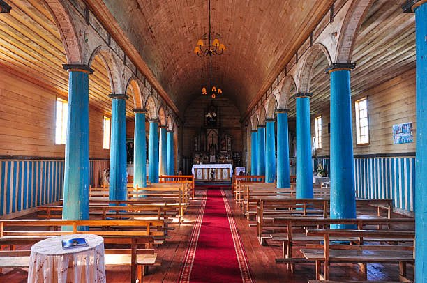 Interior de una iglesia de madera de Chiloé con columnas azules y alfombra roja