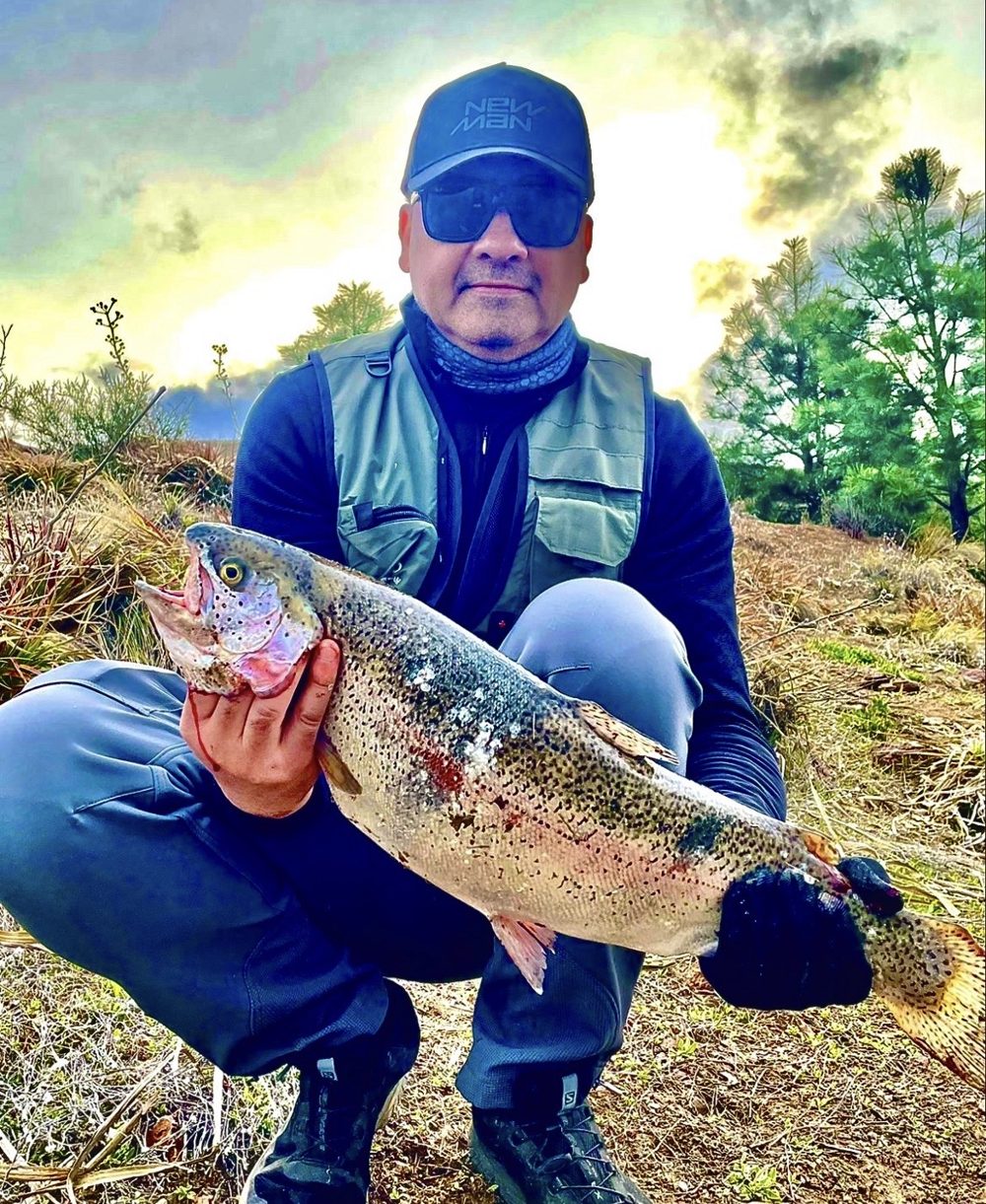 Pescador agachado con una trucha arcoíris, en Las Trampas